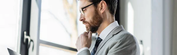 Vista laterale di un uomo d'affari premuroso che guarda il laptop in ufficio, banner — Foto stock