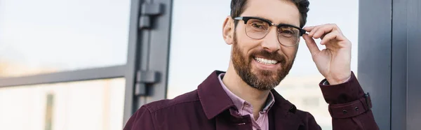 Hombre de negocios con anteojos sonriendo a la cámara cerca del edificio al aire libre, pancarta - foto de stock