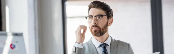 Бородатый бизнесмен в очках и костюме, стоящий в офисе, баннер — стоковое фото