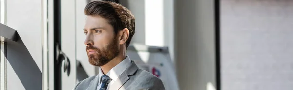 Bearded businessman in suit standing near window in office, banner — Stock Photo