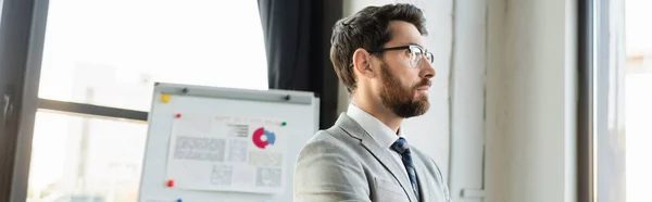 Businessman in suit looking away near flip chart in office, banner — Stock Photo