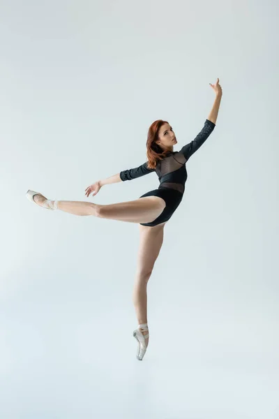 Полная длина балерины в черном телесном костюме, исполняющей танец, изолированный на сером — стоковое фото