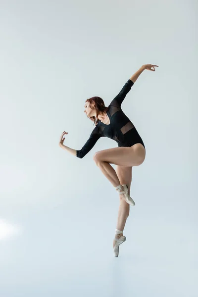 Повна довжина балерини в чорному боді-костюмі та взутті, що танцює на сірому — стокове фото