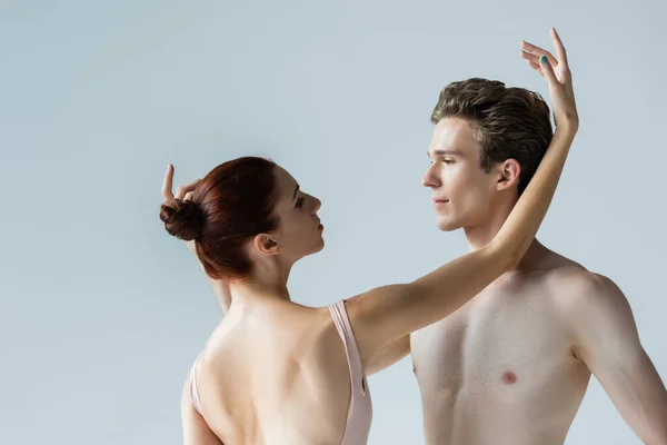 Ballerina looking at shirtless partner while performing dance isolated on grey — Stock Photo