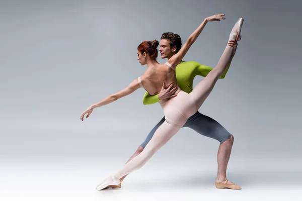 Full length of man and flexible woman performing ballet dance on grey — Stock Photo