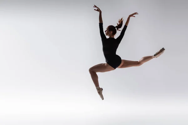 Comprimento total de bailarina jovem em bodysuit preto levitando em cinza — Fotografia de Stock