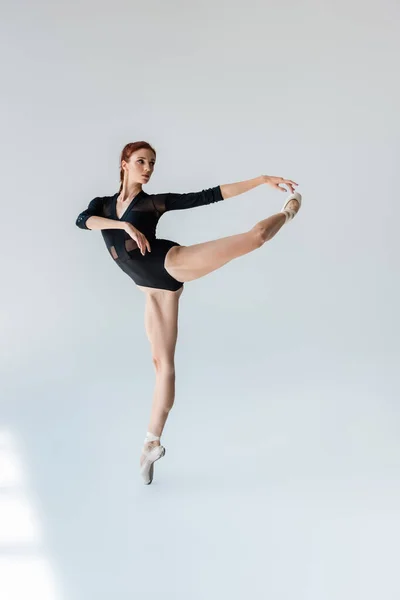 Full length of flexible ballerina in black bodysuit stretching on grey — Stock Photo