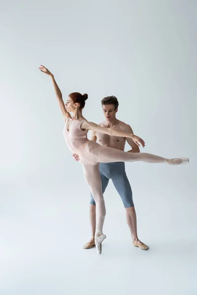 Comprimento total do homem sem camisa e mulher flexível realizando dança de balé em cinza — Fotografia de Stock