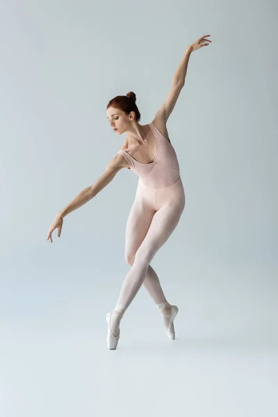 Full length of flexible and young ballerina in bodysuit dancing on grey — Stock Photo