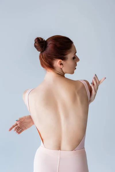 Чувственная молодая балерина в телесном костюме, обнимающая себя во время танца, изолированного на сером — стоковое фото