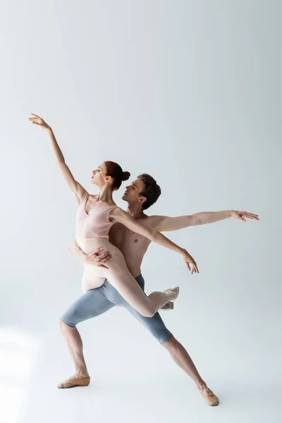 Piena lunghezza di uomo senza maglietta e donna flessibile in body che esegue danza classica su grigio — Foto stock