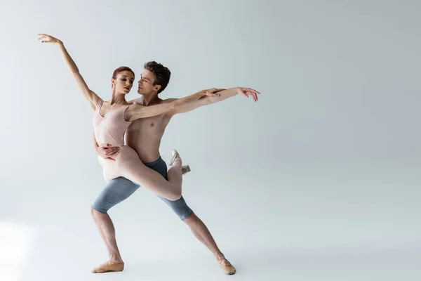Full length of shirtless man and young woman in bodysuit performing ballet dance on grey — Stock Photo