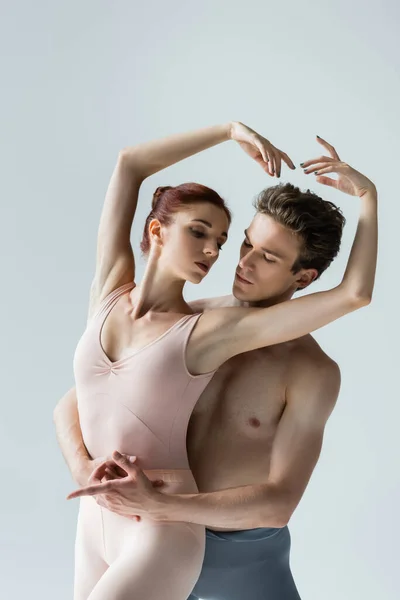 Hombre sin camisa y mujer joven con las manos levantadas realizando danza de ballet aislado en gris - foto de stock