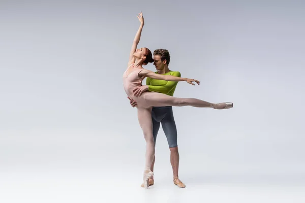 Longitud completa de hombre y mujer jóvenes con la mano levantada realizando danza de ballet en gris - foto de stock