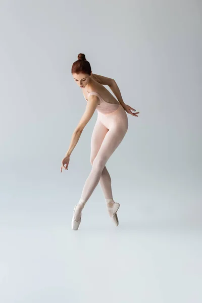 Full length of sensual ballerina in pointe shoes and bodysuit dancing on gray — Stock Photo