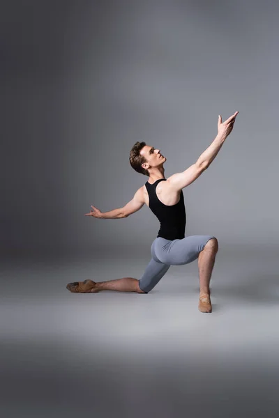 Young ballet dancer in black tank top performing ballet dance while standing on knee on dark grey — Stock Photo