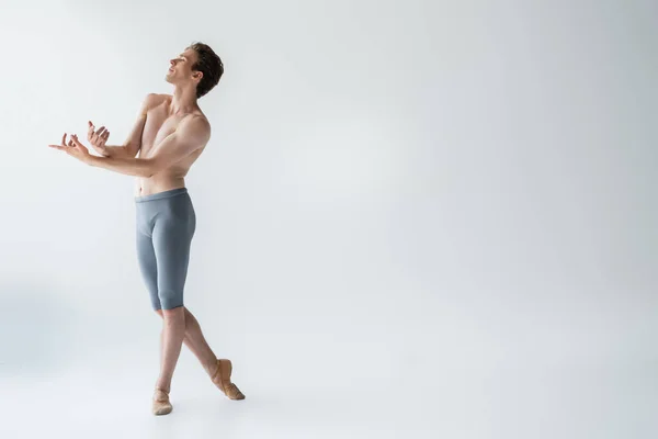 Toute la longueur du danseur de ballet torse nu exécutant la danse sur gris — Photo de stock