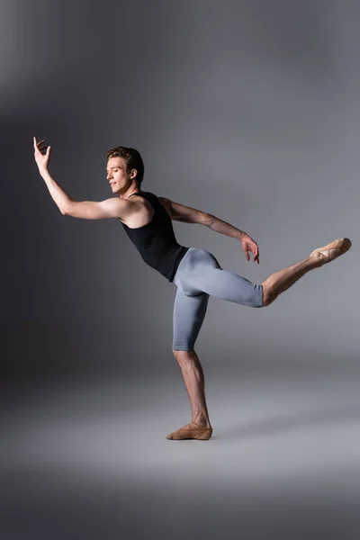 Toute la longueur du danseur de ballet gracieux en débardeur gestuelle sur gris foncé — Photo de stock