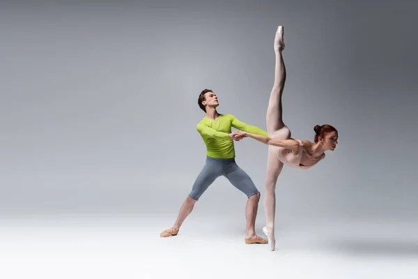 Toute la longueur du danseur de ballet soutenant la ballerine pendant la danse sur gris foncé — Photo de stock