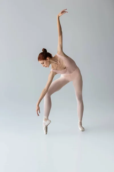 Full length of ballerina in ballet shoes dancing with outstretched hand on grey — Stock Photo