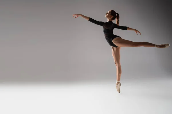 Full length of woman in ballet shoes dancing with outstretched hands on dark grey — Stock Photo