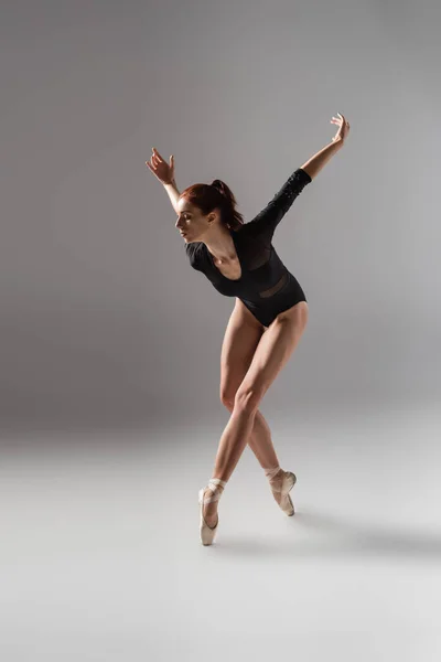 Полная длина молодой женщины в балетных туфлях танцующих с протянутыми руками на темно-серой — стоковое фото