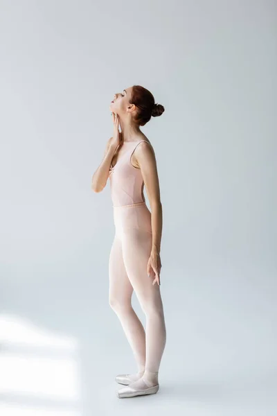 Full length of elegant ballerina in ballet shoes touching neck on grey — Stock Photo