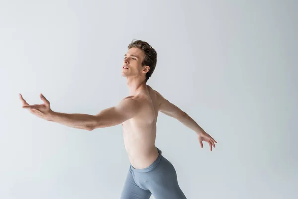 Молодой балетный танцор без рубашки исполняет танец изолированный на сером — стоковое фото