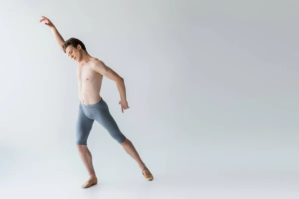По всей длине молодой танцовщицы без рубашки, исполняющей балетный танец на сером — стоковое фото