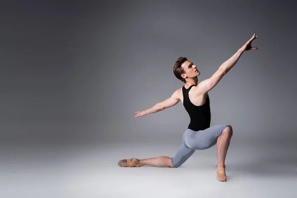 Larga duración de la joven bailarina de ballet en camiseta sin mangas bailando sobre gris oscuro - foto de stock