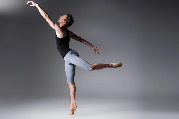 Toute la longueur du danseur de ballet gracieux exécutant la danse de ballet sur le gris foncé — Photo de stock