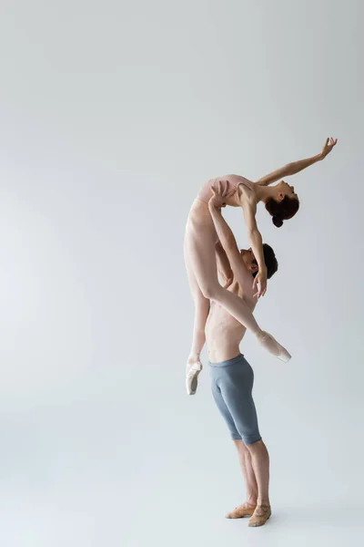 Longitud completa de bailarina de ballet sin camisa levantando joven bailarina en gris - foto de stock