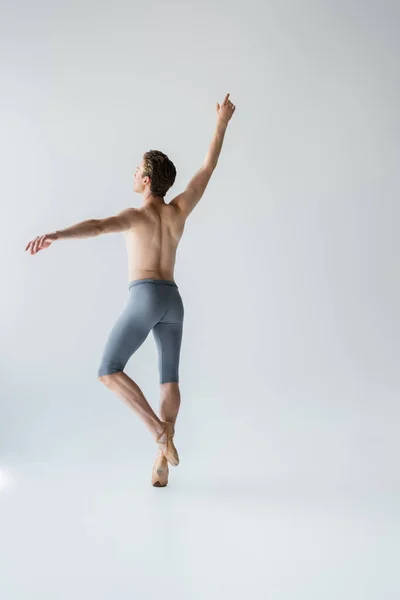 Jovem bailarino sem camisa com a mão levantada no cinza — Fotografia de Stock