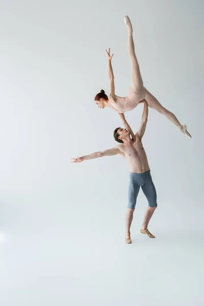 Longueur totale de danseuse de ballet torse nu soulevant gracieuse ballerine en body sur gris — Photo de stock