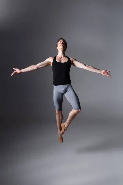 Toute la longueur du danseur de ballet élégant effectuant lévitation avec les mains tendues sur le gris foncé — Photo de stock