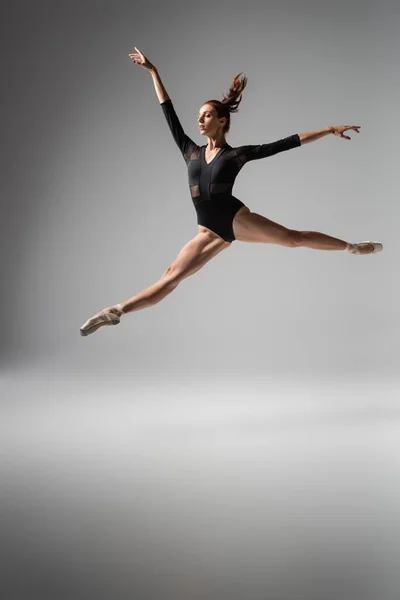 Bailarina ligera en zapatos puntiagudos y body negro saltando sobre gris oscuro - foto de stock