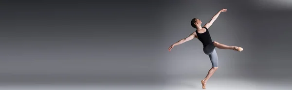 Longitud completa de hombre elegante realizando danza de ballet en gris oscuro, bandera - foto de stock