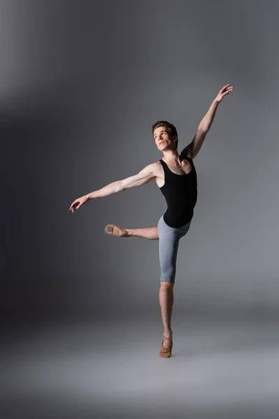 Volle Länge des eleganten Mannes in Ballettschuhen, der Balletttanz auf dunkelgrau vorführt — Stockfoto
