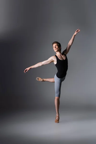 Full length of elegant man in ballet shoes performing ballet dance on dark grey — Stock Photo