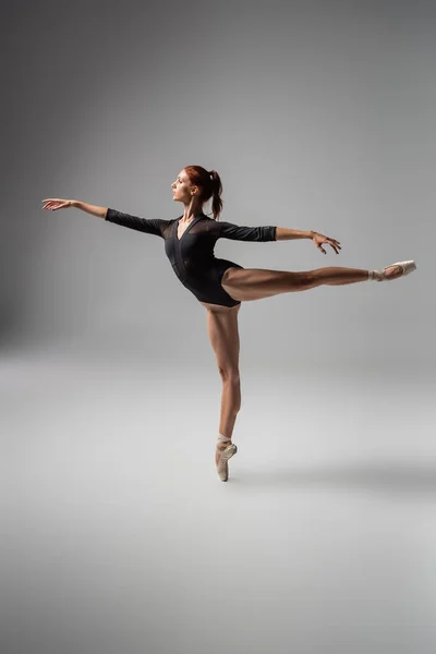 Full length of pretty woman in ballet shoes performing ballet dance while standing on pointe shoe on dark grey — Stock Photo