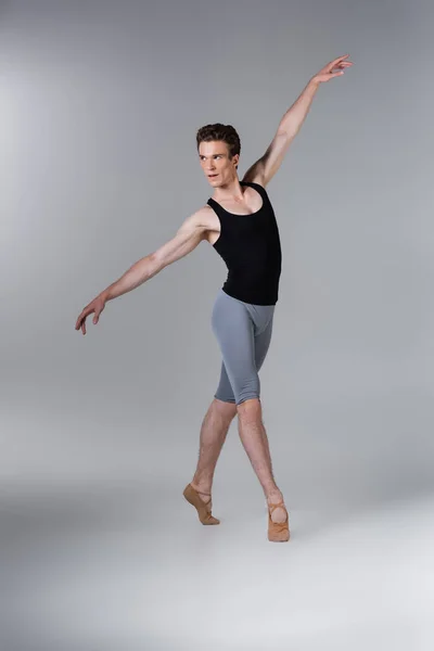 Pleine longueur de jeune homme en chaussures de ballet exécutant danse de ballet sur gris — Photo de stock