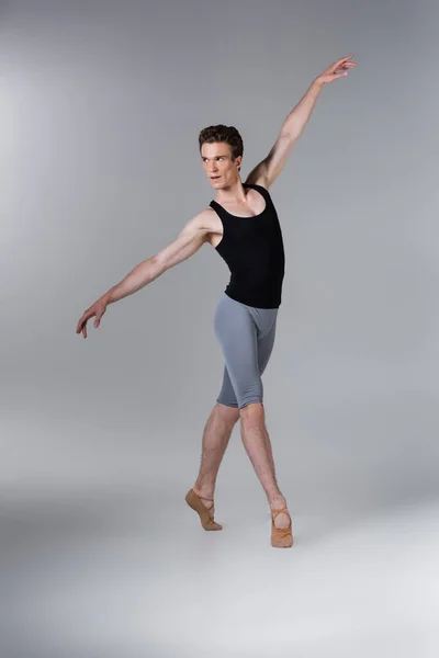 Full length of young man in ballet shoes performing ballet dance on grey — Stock Photo