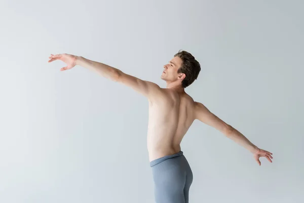 Jovem sem camisa com as mãos estendidas realizando dança de balé isolado no cinza — Fotografia de Stock