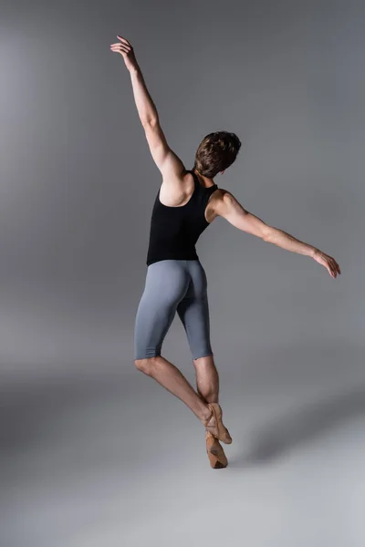 Back view of young man in ballet shoes performing ballet dance on dark grey — Stock Photo