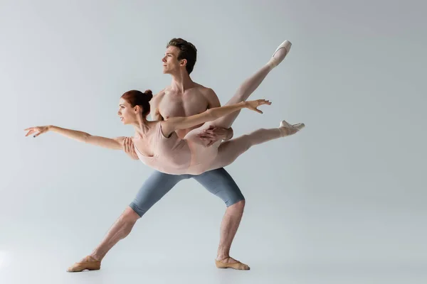 Bailarina de ballet sin camisa levantando joven bailarina aislada en gris - foto de stock