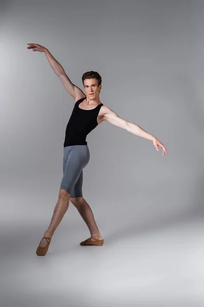 Joven y elegante bailarina de ballet haciendo gestos mientras realiza danza de ballet en gris oscuro - foto de stock