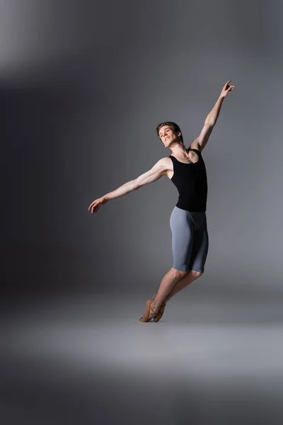 Danseuse gracieuse avec les mains tendues exécutant danse de ballet sur gris foncé — Photo de stock