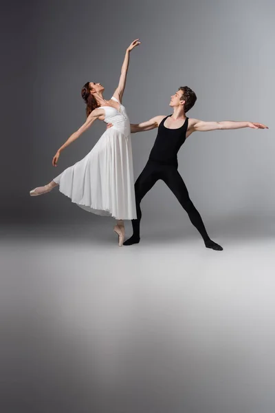 Comprimento total de bailarina graciosa no vestido branco dançando com o parceiro no cinza escuro — Fotografia de Stock