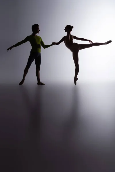 Вид сбоку изящной балерины в боди-костюме танцующей с партнером по темно-серой — стоковое фото