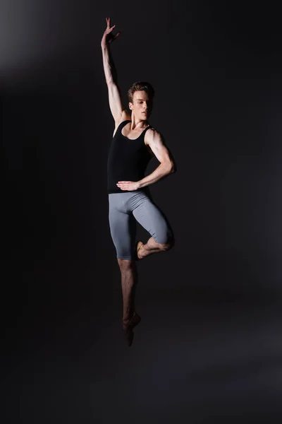 Joven y elegante bailarina haciendo gestos mientras realiza danza de ballet mientras salta sobre negro - foto de stock
